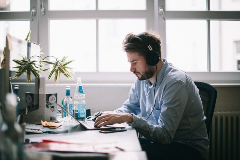 Professional working at a desk using a laptop while wearing headphones, focused on monitoring internal controls and compliance tasks. The office setting with documents and digital tools highlights risk management, regulatory compliance, and corporate governance oversight.
