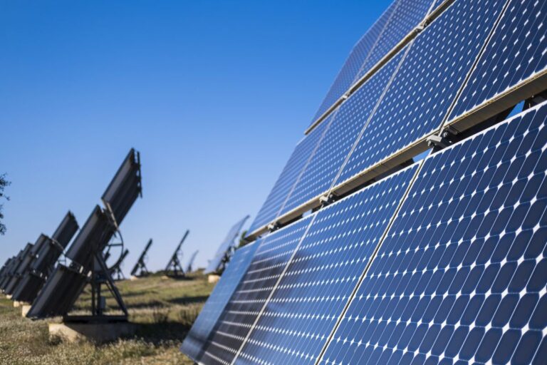Close up view of large solar panels installed in an outdoor array under a clear blue sky. The angled photovoltaic modules highlight renewable energy generation and sustainable solar power solutions.