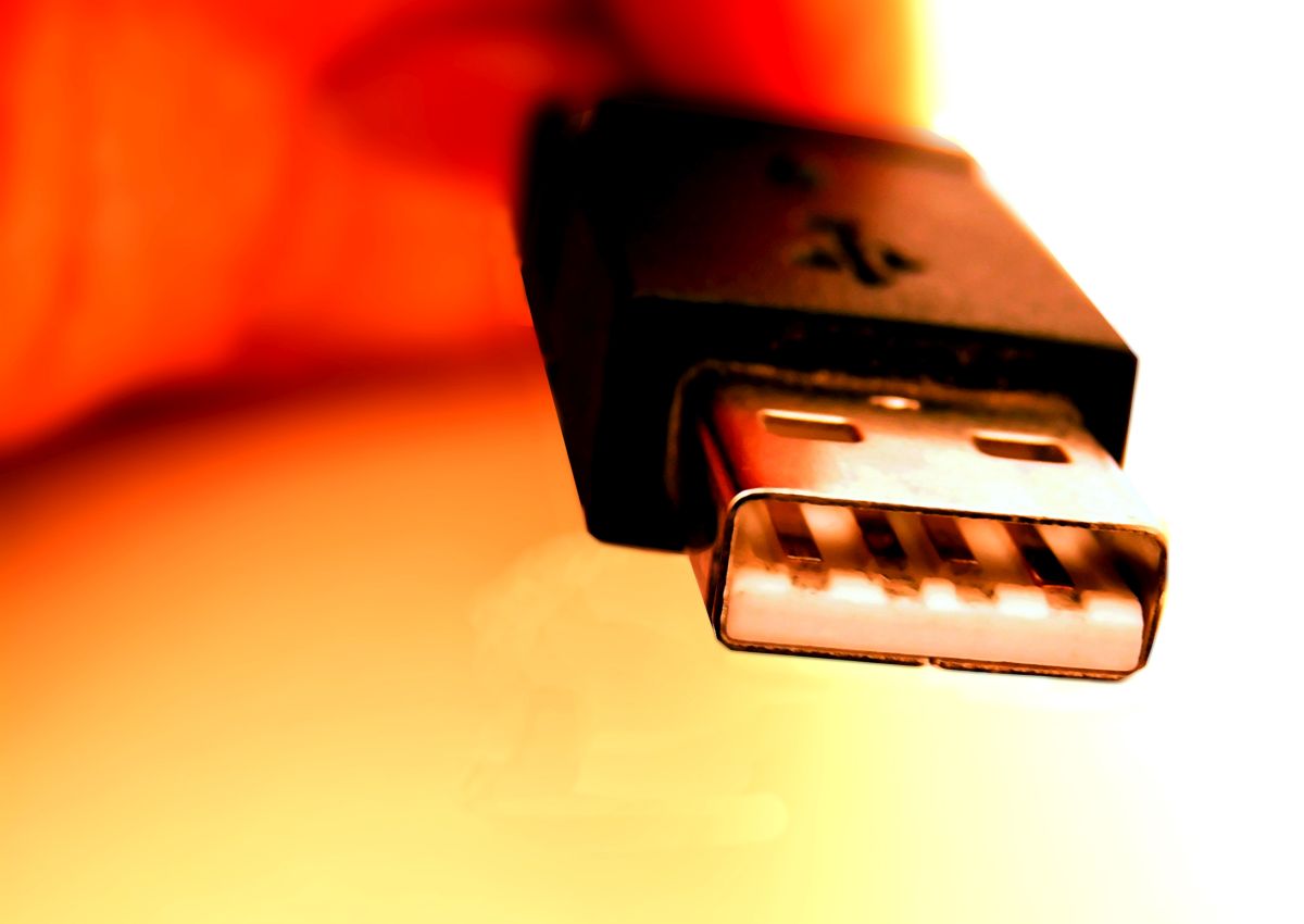 Close up of a USB connector plug making a connection, with metal contacts clearly visible against a warm orange background. The image highlights data transfer hardware and potential cybersecurity risks from infected USB devices.