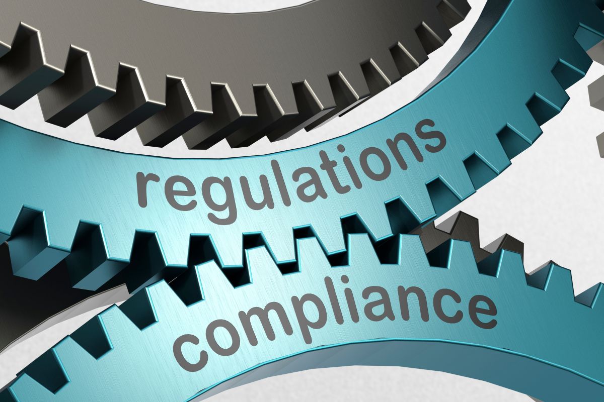 Close up 3D rendering of interlocking metal gears engraved with the words regulations and compliance. The connected gears symbolize how regulatory requirements and compliance processes work together within an organization.