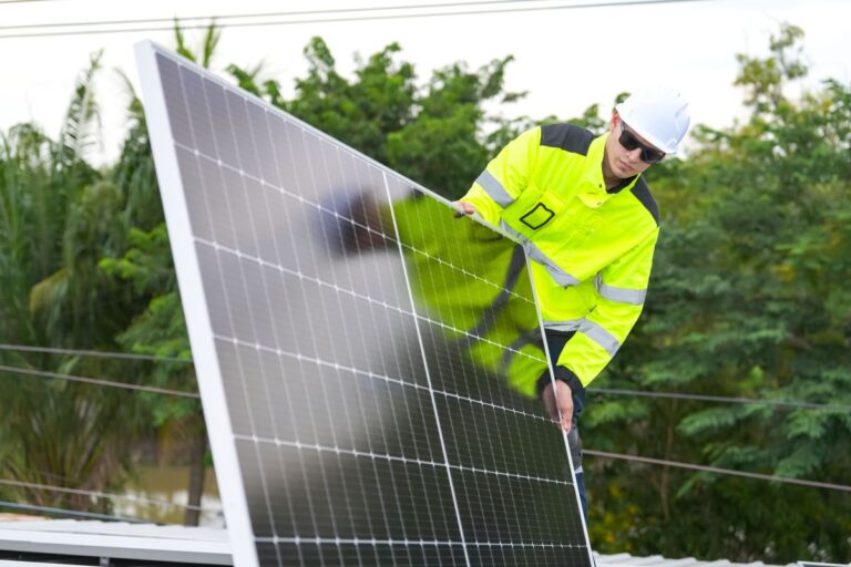 MenTechniciansMountingPhotovoltaicSolarModulsOnRoofOfHouse Technician in a hard hat and high visibility jacket mounting a photovoltaic solar panel on the roof of a house. The worker carefully positions the solar module, highlighting residential solar installation and community renewable energy adoption.