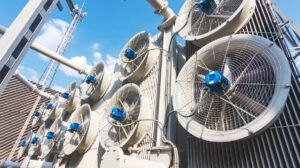 Industrial cooling fans mounted on the side of a large power transformer at an electrical substation. Blue motor housings and metal grilles highlight the equipment used to regulate temperature and support grid reliability.