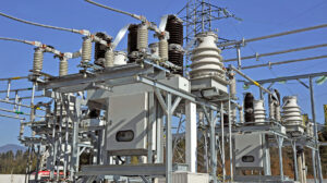 Electrical substation equipment with transformers, insulators, and high voltage lines mounted on steel structures against a clear blue sky. The image represents power system infrastructure supporting compliance with VAR 002 voltage and reactive power requirements.