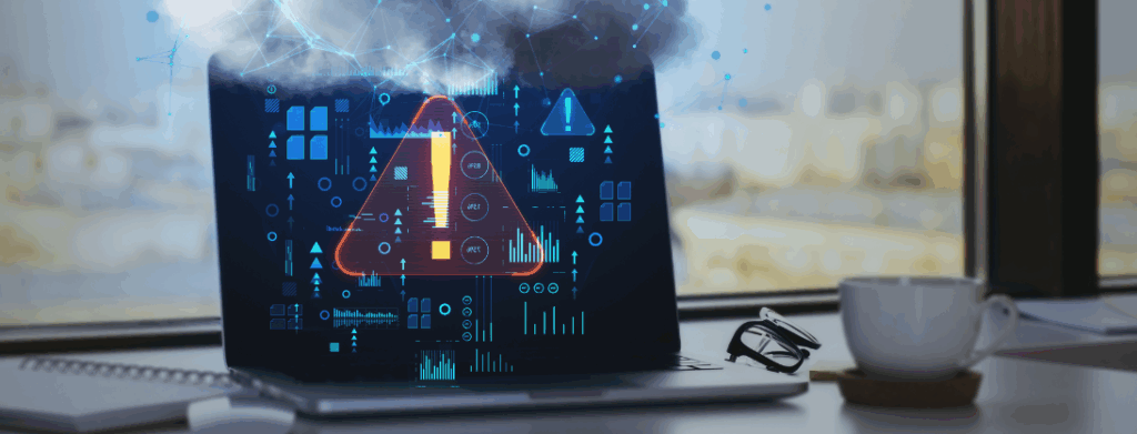 Laptop on a desk displaying a large warning symbol and cybersecurity data graphics on the screen, with smoke rising from the device. The image represents ransomware as an imminent threat to power generation facilities and critical infrastructure systems.