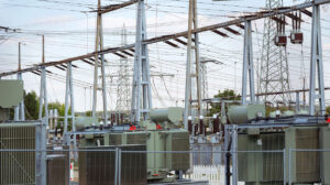 lectrical substation with large power transformers, high voltage busbars, and a network of transmission lines supported by steel structures. The complex grid infrastructure represents evolving NERC CIP standards, critical asset protection, and cybersecurity compliance for bulk electric system facilities.