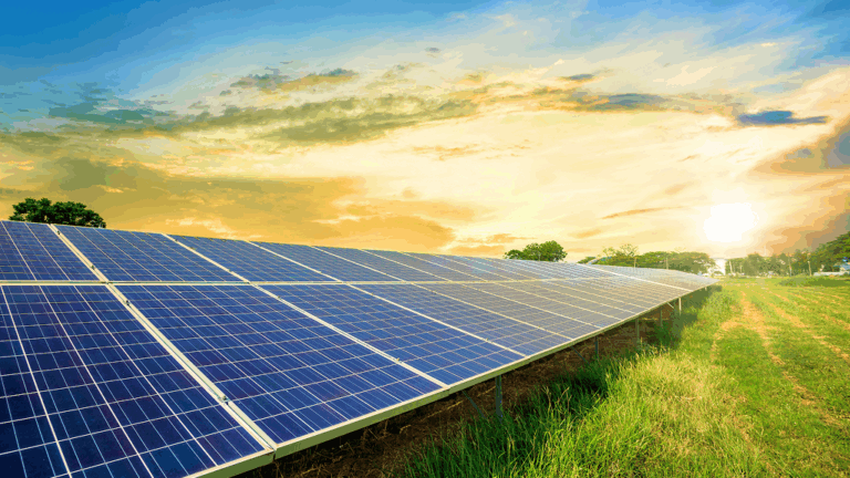 Wide view of a solar panel array installed on a grassy field at sunset, with golden light illuminating the photovoltaic modules. The clean energy landscape represents grid connected renewable resources and compliant integration of inverter based resources within modern power systems.