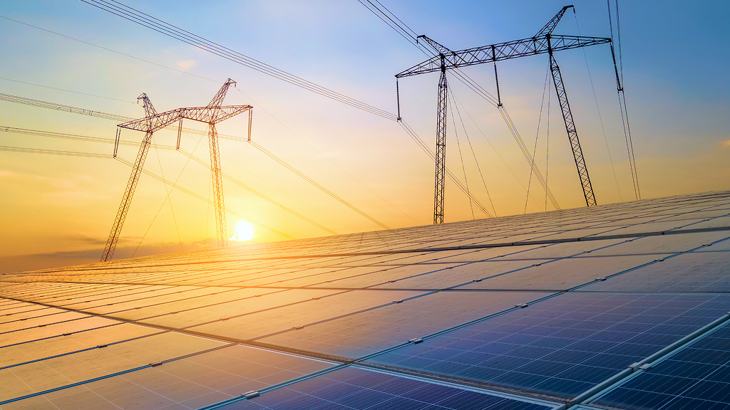 Information Guide - FAC-008 Extended Common Questions and Answers - Feature Image Wide-angle image of a solar panel field at sunset with high-voltage transmission towers and power lines stretching across the sky. The scene symbolizes the intersection of renewable energy and grid infrastructure, relevant to FAC-008 transmission reliability standards.
