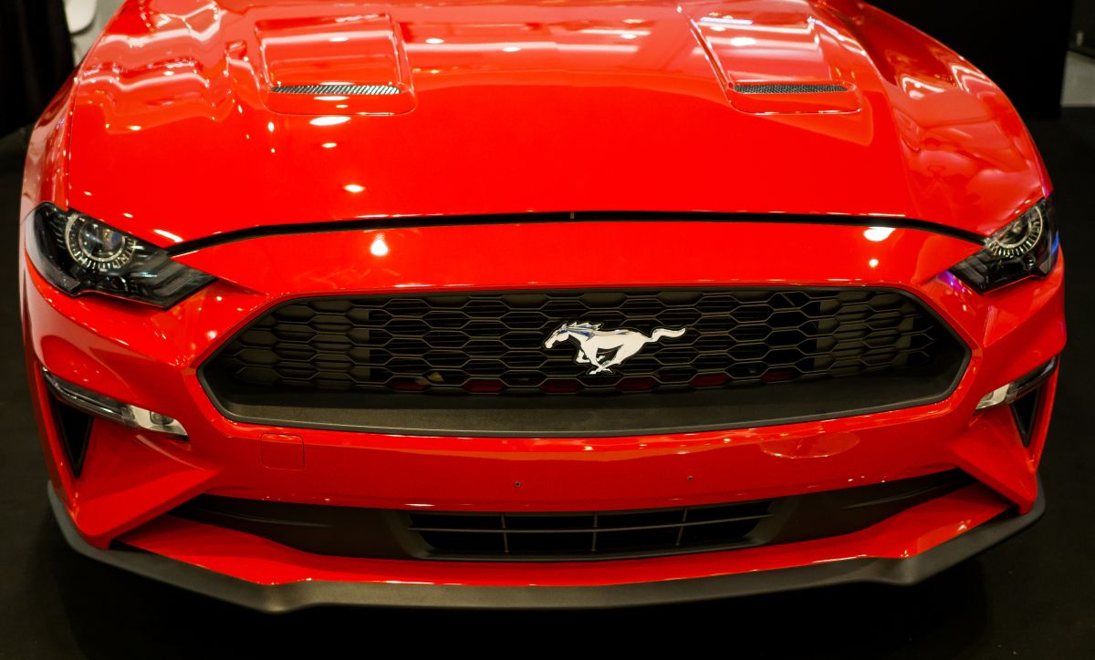 Front view of a red Ford Mustang with the chrome pony emblem centered on a black grille. The close up highlights the sporty design, headlights, and bold red hood of the performance car.