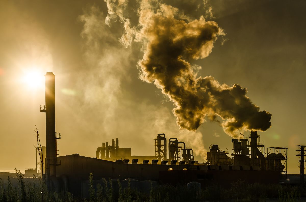 Factory smokestacks releasing thick air pollution into the sky during a dramatic sunset. Dark smoke billows above the industrial facility, silhouetted against golden sunlight, highlighting global environmental and carbon emission concerns.
