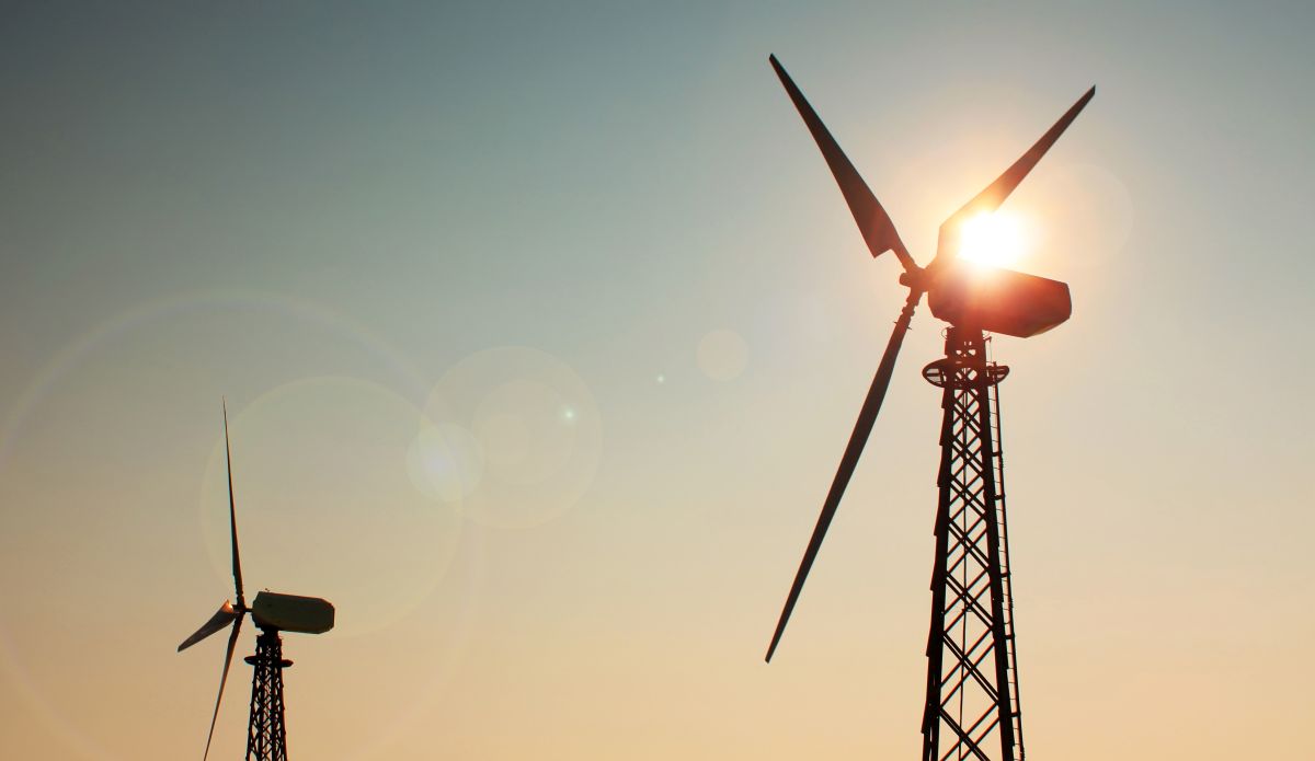 Silhouette of windmills at sunset with the sun shining through the blades.