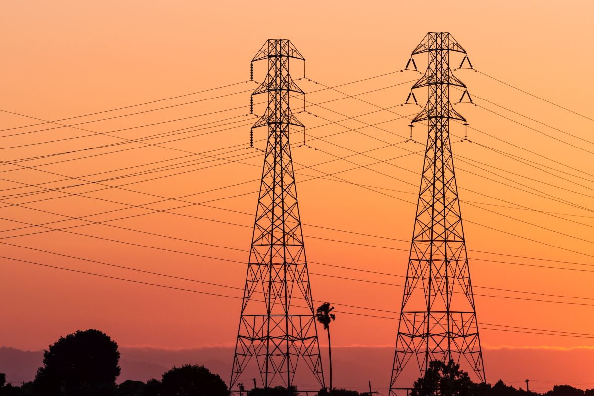 High-voltage electricity towers silhouetted against a vibrant sunset sky, with power lines stretching across the horizon.