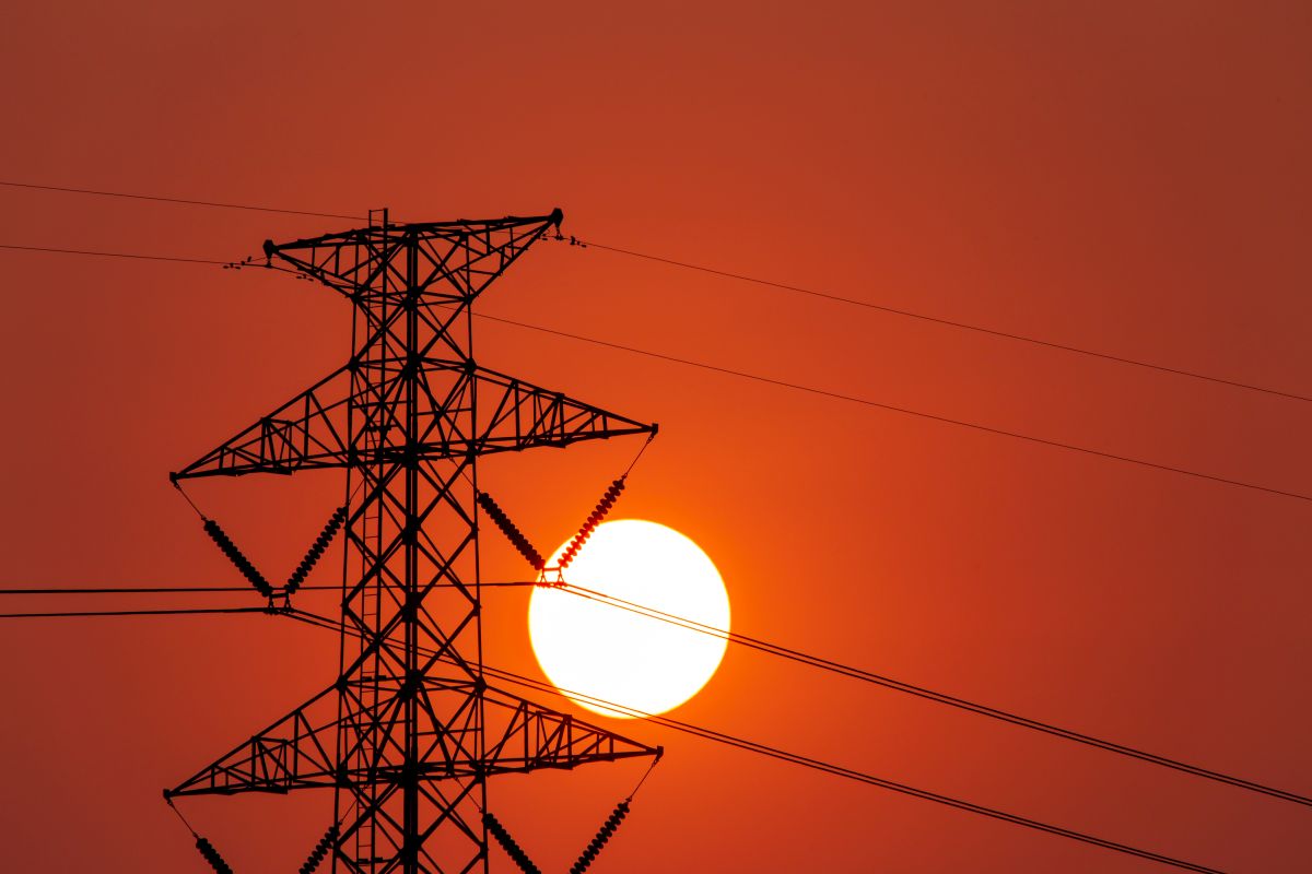 silhouette of high voltage electrical pole structure Silhouette of a high-voltage electrical transmission tower with power lines against the backdrop of a large sun setting in the sky.