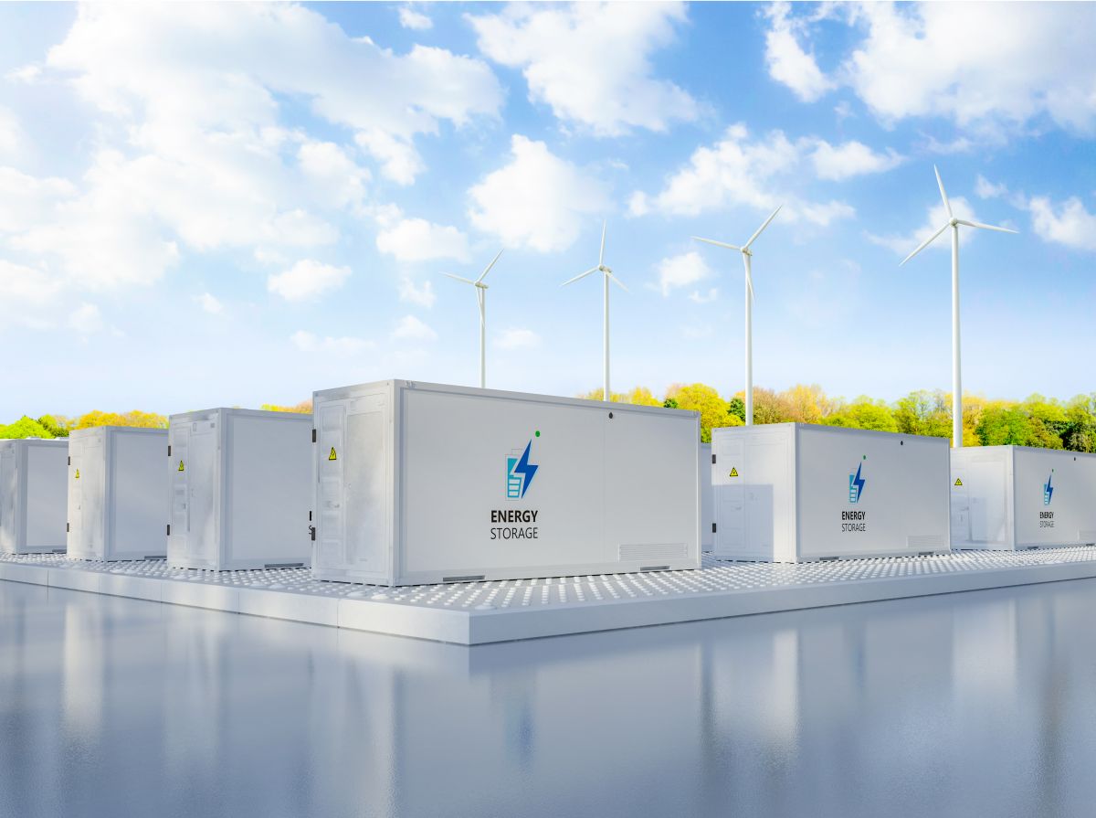 Energy storage units in the foreground with wind turbines in the background, under a bright blue sky with scattered clouds.