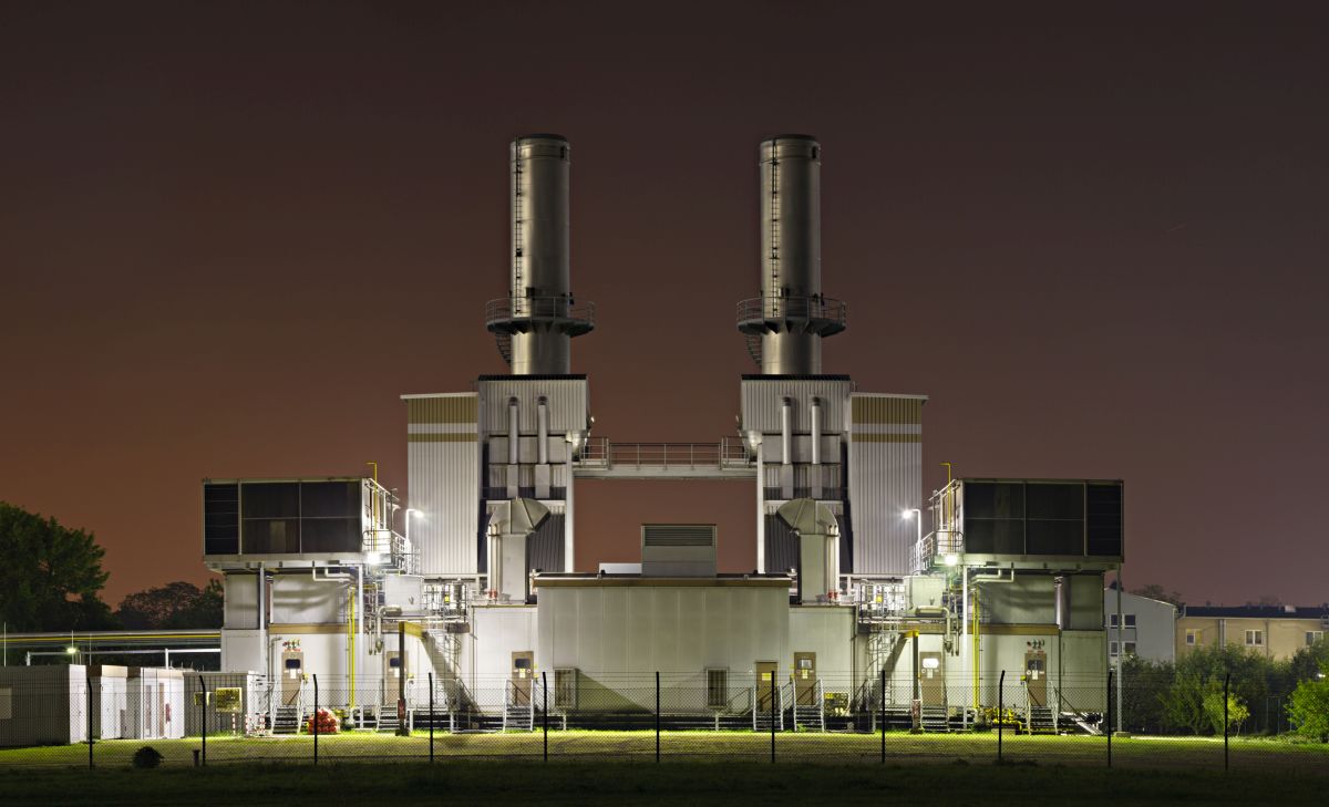 Industrial building at night with large power generation units and smokestacks, illuminated by security lights.