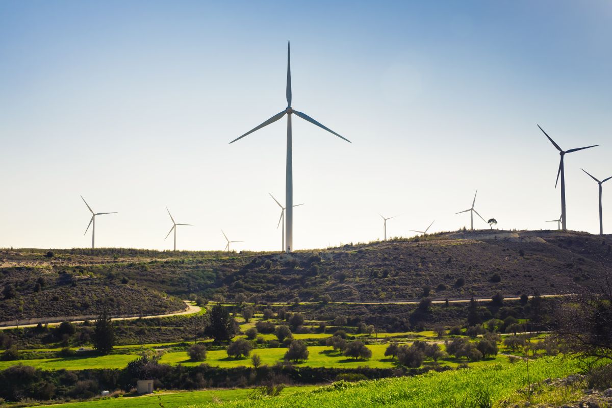 Wind turbines generating electricity across a green meadow and rolling hills under a clear sky. The image highlights renewable wind energy infrastructure integrated into a natural landscape.