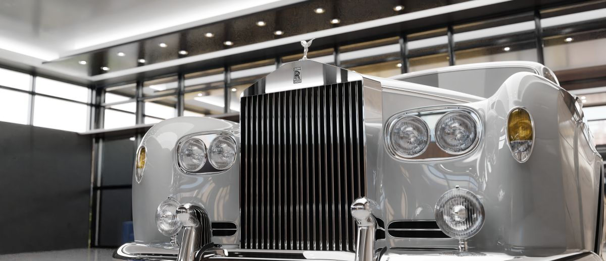 Front view of a classic Rolls Royce Silver Cloud with a polished chrome grille and round headlights displayed indoors, highlighting luxury car design details.