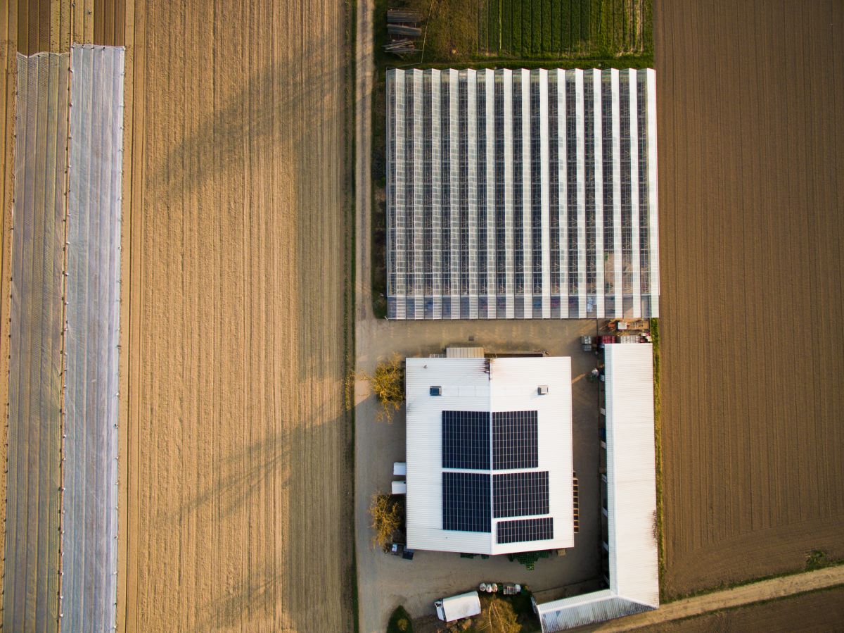 Aerial view of a field greenhouse and a house with solar panels on the roof in Germany, surrounded by farmland.