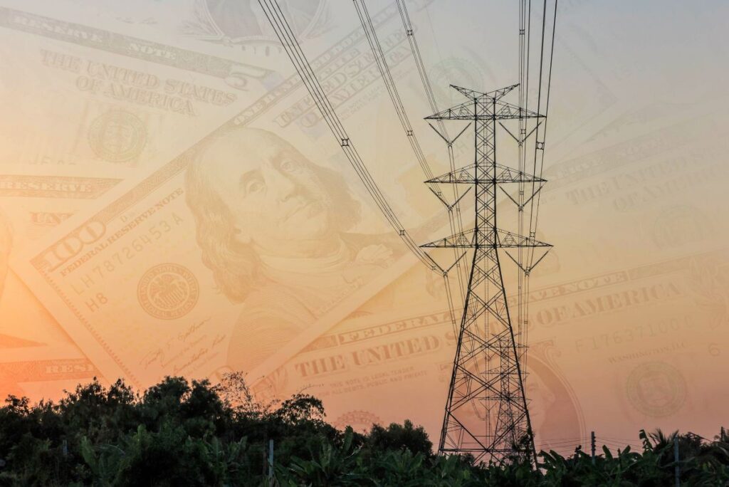 The image shows a power transmission tower with electric lines in the foreground, and a blurred background featuring dollar bills, symbolizing the connection between electricity and financial value.