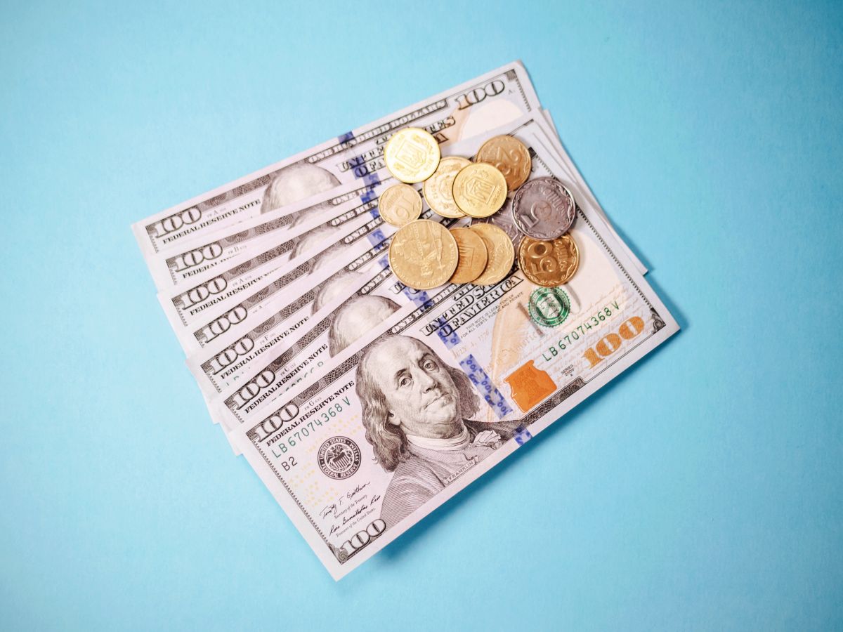 Stack of US one hundred dollar bills with assorted coins placed on top against a blue background, representing funding or financial investment.