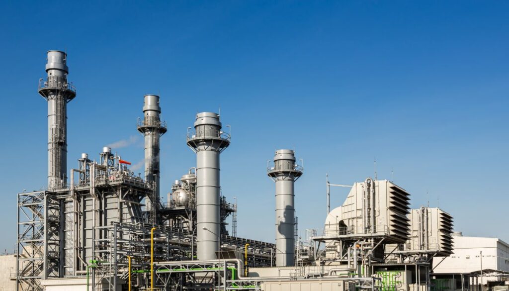 Power plant with tall metal stacks and industrial piping under a clear blue sky.