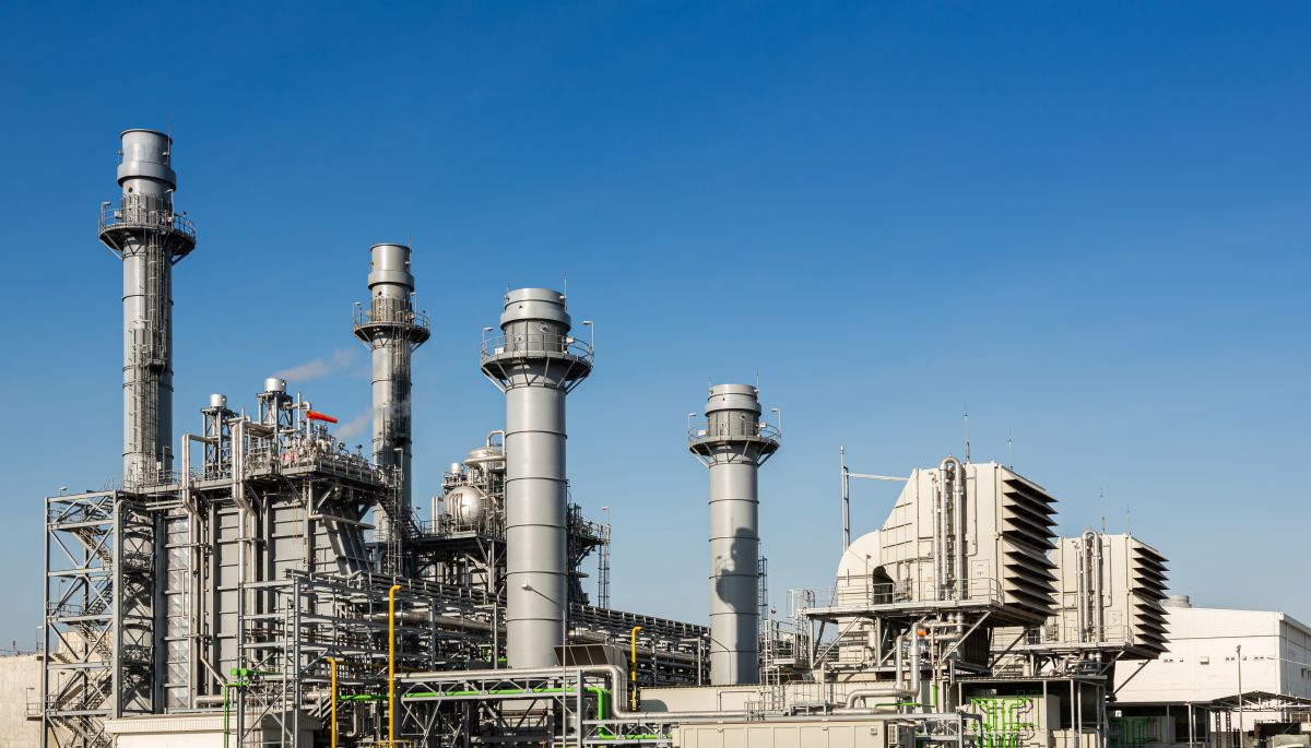 Power plant with tall metal stacks and industrial piping under a clear blue sky.