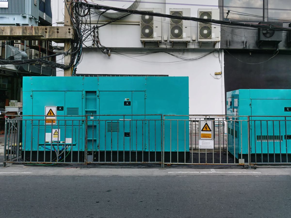 Mobile emergency electric power generator units secured behind a metal fence at an industrial site. The image highlights temporary on site generation equipment used to support grid reliability during power shortfalls or outages.