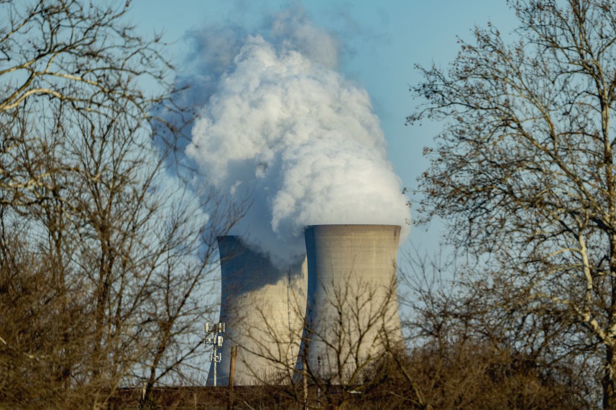 Steam coming out from the nuclear power plants Two large cooling towers release thick white steam into the sky at a nuclear power plant, partially obscured by bare winter trees in the foreground. The contrast of industrial infrastructure and natural surroundings emphasizes the plant's environmental presence.
