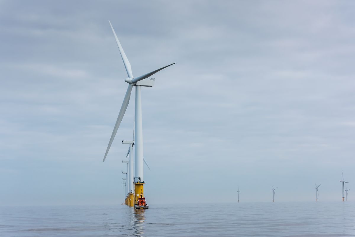 Offshore wind turbines rising from the sea viewed from a service boat on calm water under an overcast sky. The image highlights offshore wind farm infrastructure generating renewable energy in a marine environment.