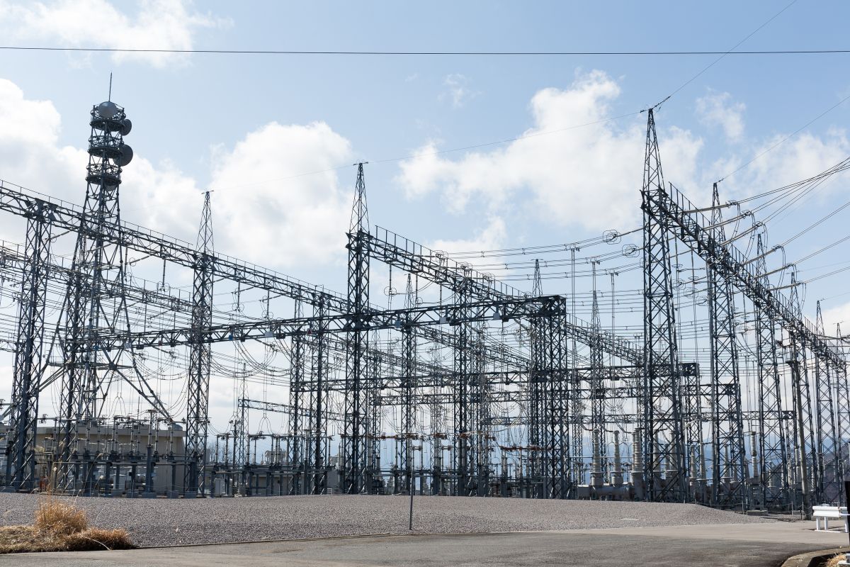 Electrical substation with steel towers and power lines under a partly cloudy sky.