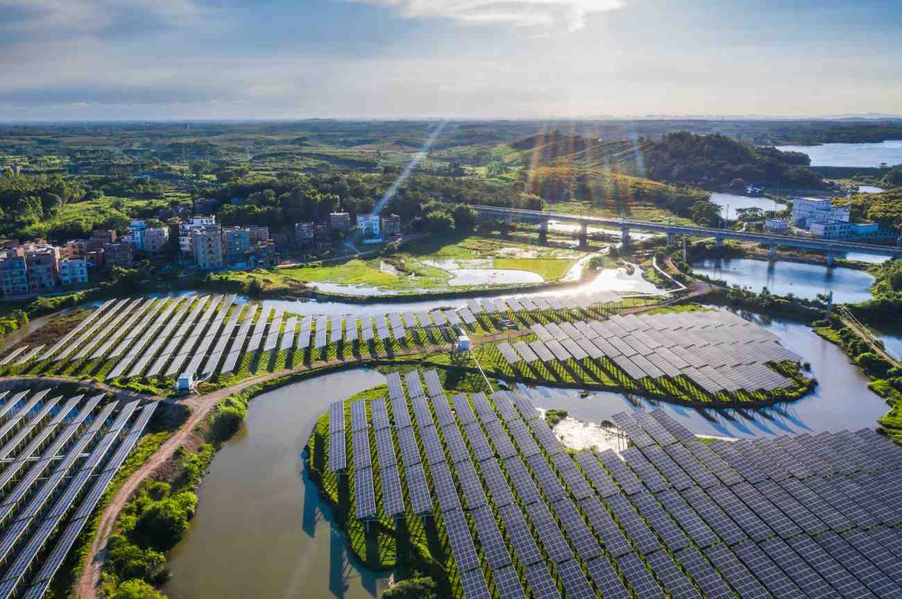 Aerial view of a large solar farm beside water channels and a bridge in a green landscape.