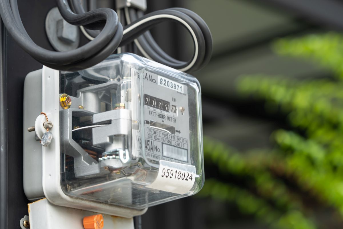 Close-up of an electric power meter used to measure energy consumption, mounted on a wall with electrical wires attached.