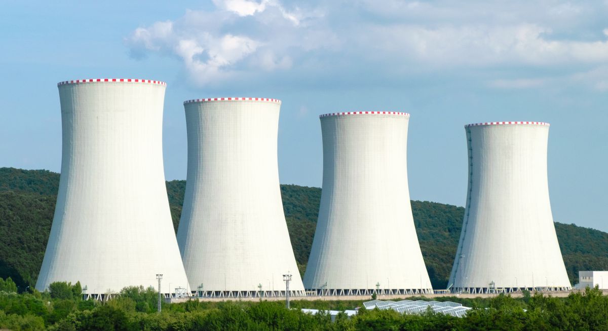 Nuclear power plant cooling towers with a backdrop of a clear blue sky and green mountains.