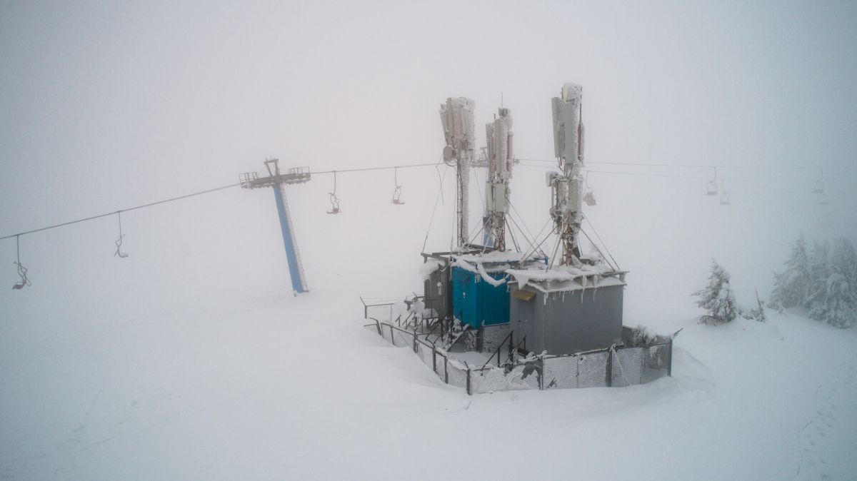 Snow and ice-covered mobile station in a winter landscape, with a ski lift in the background, highlighting winter grid reliability.