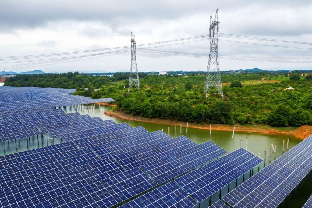 Floating solar panels installed on a body of water with transmission towers and power lines overhead. The image highlights energy security and infrastructure upgrades supporting renewable power integration.