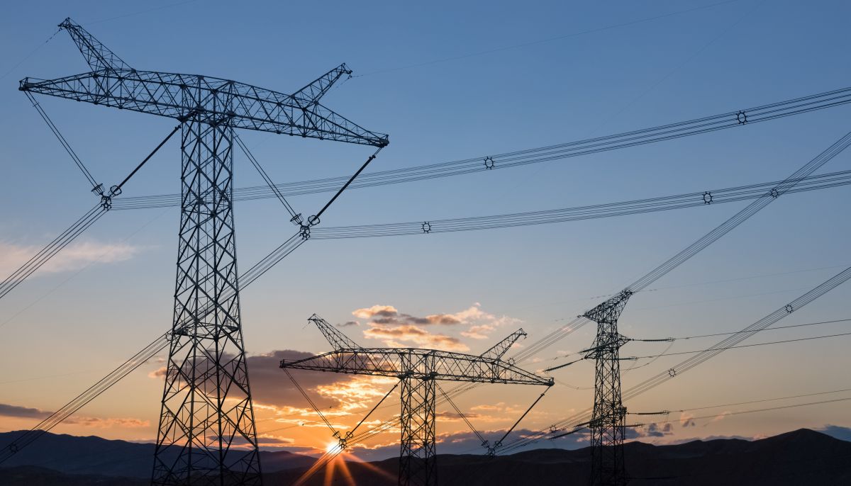 Power transmission pylons silhouetted against a sunrise, symbolizing the transmission infrastructure in the energy sector.