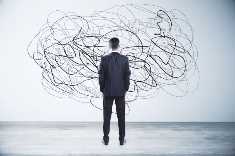 The image shows a man in a suit standing in front of a chaotic, tangled line drawing on the wall, symbolizing confusion or complexity.