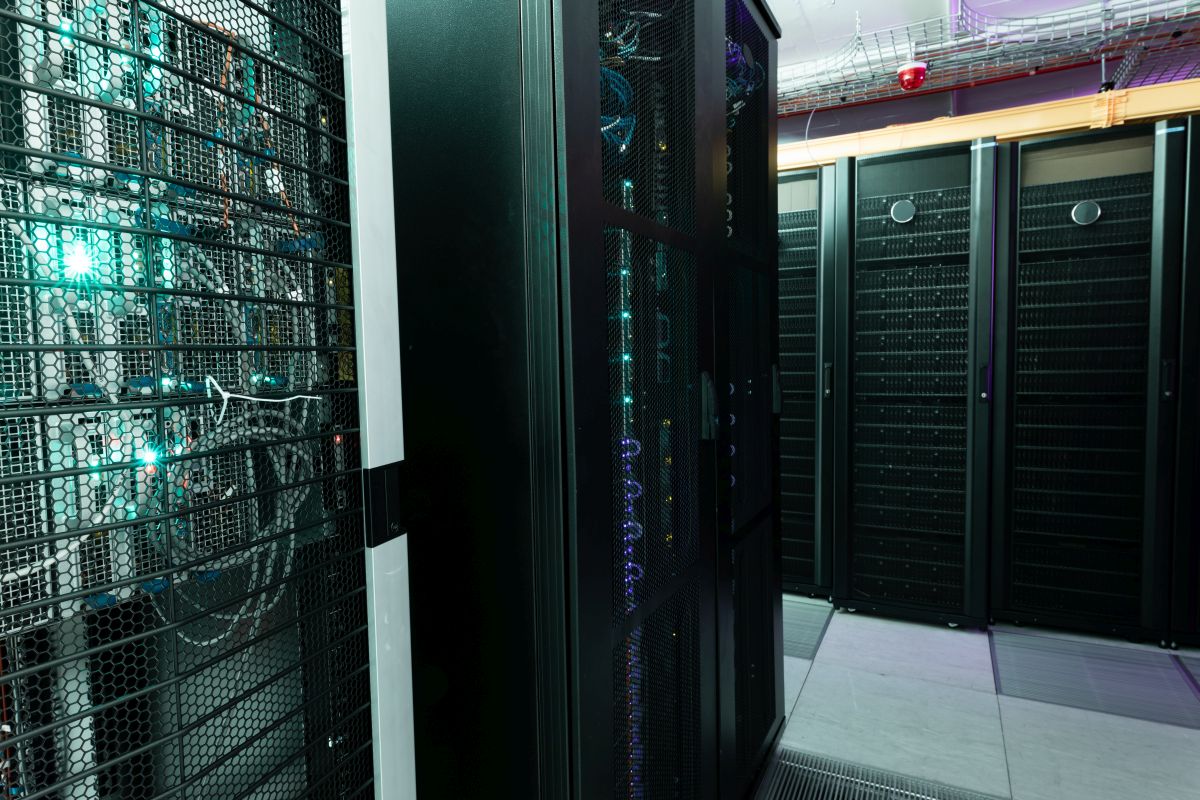 Multiple rows of fully operational server racks inside a modern data center with visible cabling and network equipment. The image represents cloud computing infrastructure and secure data center operations supporting digital services.