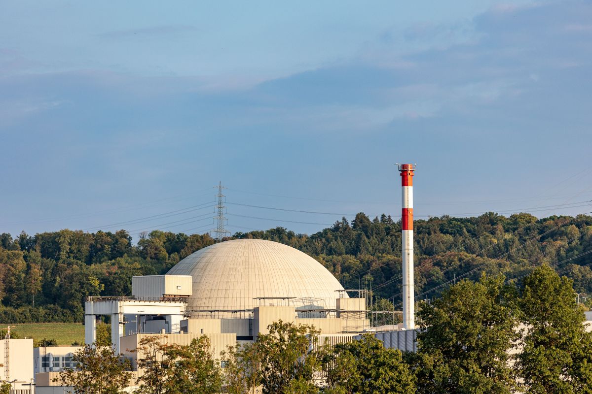 Neckarwestheim Nuclear Power Plant in Germany featuring a large reactor dome and industrial chimney surrounded by trees and power lines. The image highlights active nuclear energy infrastructure in a rural landscape.