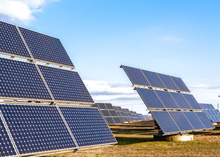 Rows of solar panels angled toward the sun at a solar power plant under a clear blue sky. The image highlights renewable energy generation using photovoltaic technology.