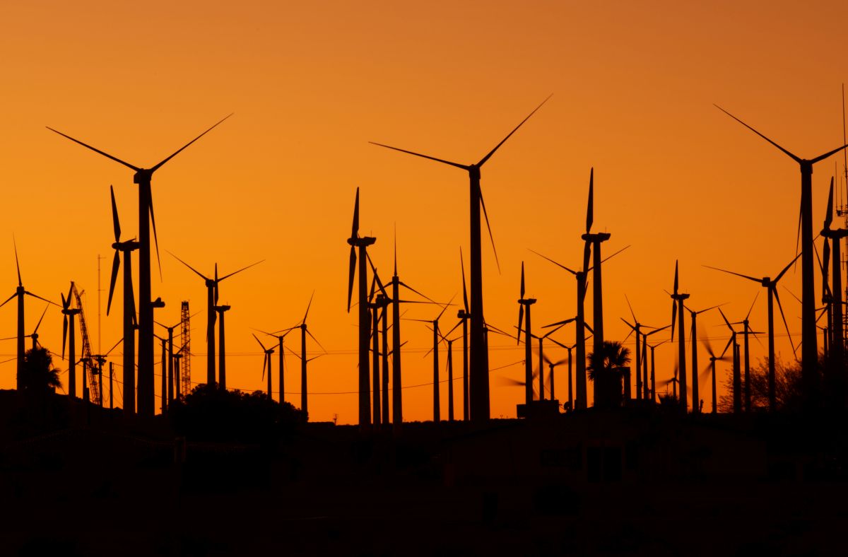 A silhouette of multiple wind turbines against a vibrant orange sunset sky.