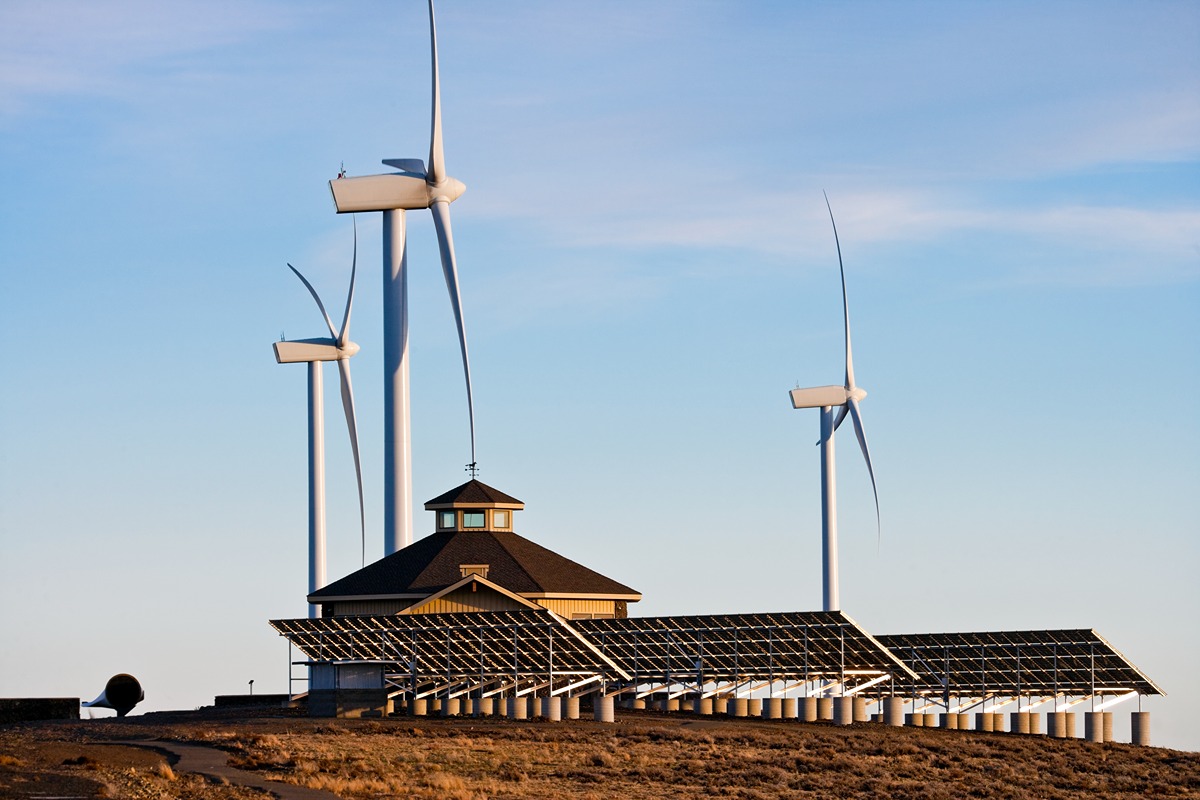 A hybrid renewable energy facility featuring wind turbines and a large solar panel array surrounding a central building under a clear sky. The image represents the partnership between Sunrun and NRG Energy to expand distributed energy in Texas.