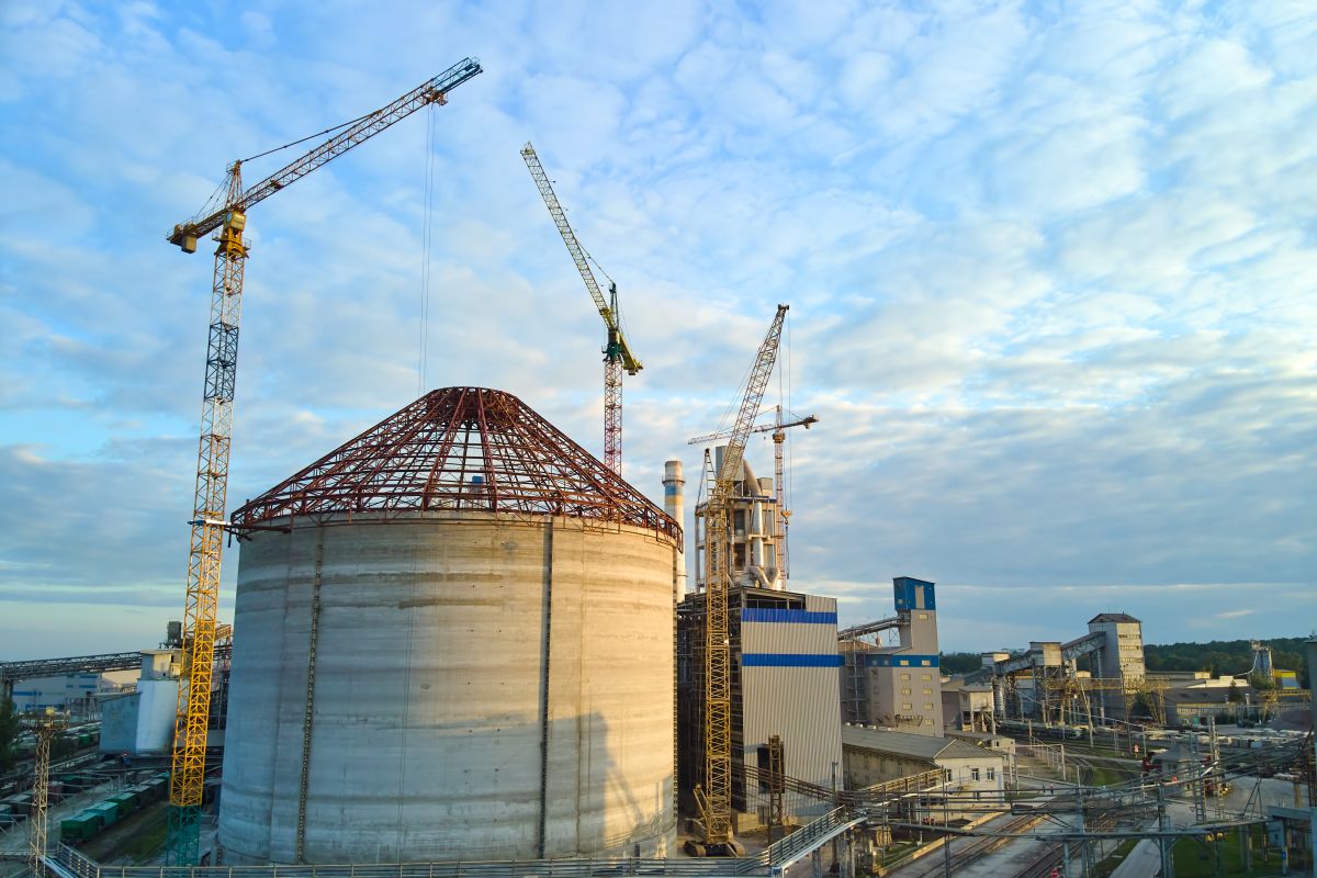Aerial view of a cement factory under construction with large concrete structures and tower cranes at an industrial production site.