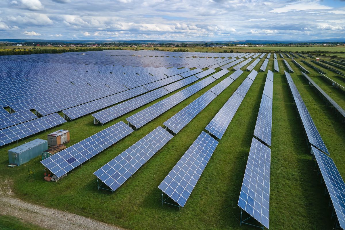 Aerial view of a large sustainable solar power plant with rows of solar panels on a grassy field.