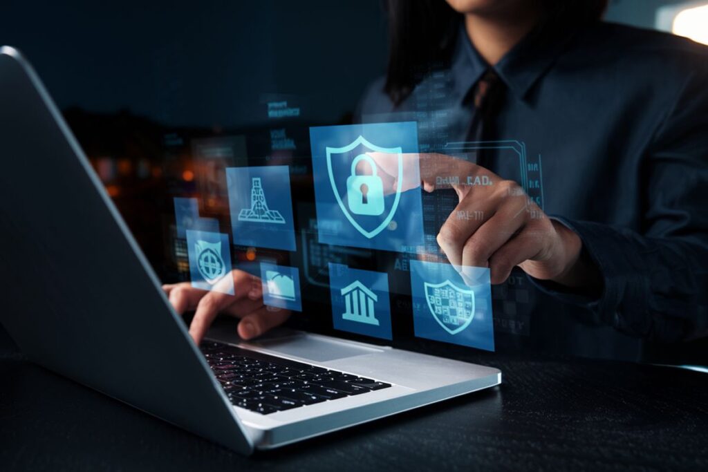 Person interacting with a digital touchscreen interface above a laptop, selecting icons related to cybersecurity such as a shield with a padlock. The image illustrates implementing digital security management controls in compliance frameworks.