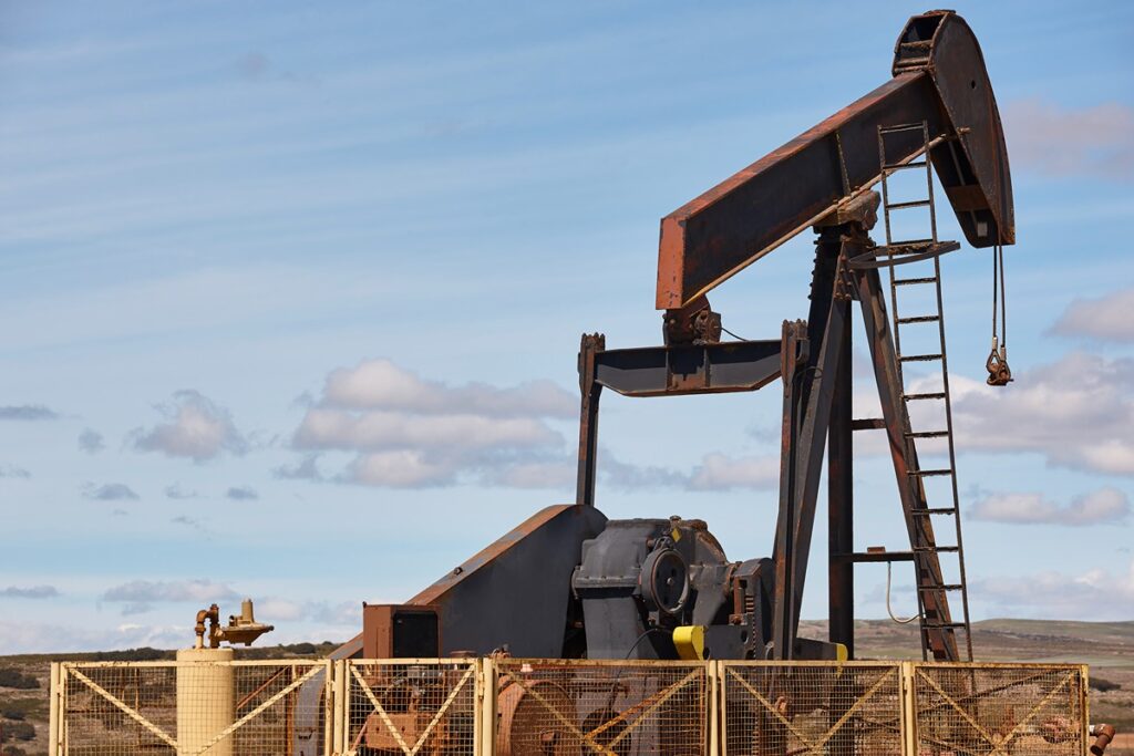 Rusted oil pumpjack operating in an open landscape under a partly cloudy sky, surrounded by a safety fence. The image reflects crude oil extraction, relevant to U.S. licensing changes on Venezuelan oil exports.