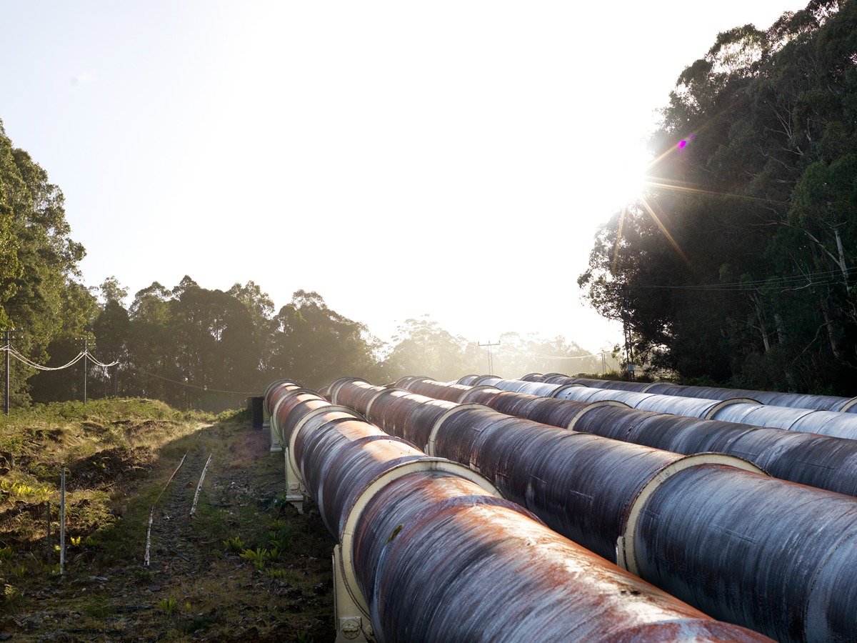 Large metal pipeline sections laid out in a forest clearing, catching the morning sun with trees and power lines in the background. The image represents infrastructure development tied to the approved 55-mile Transco Southeast supply enhancement pipeline project.