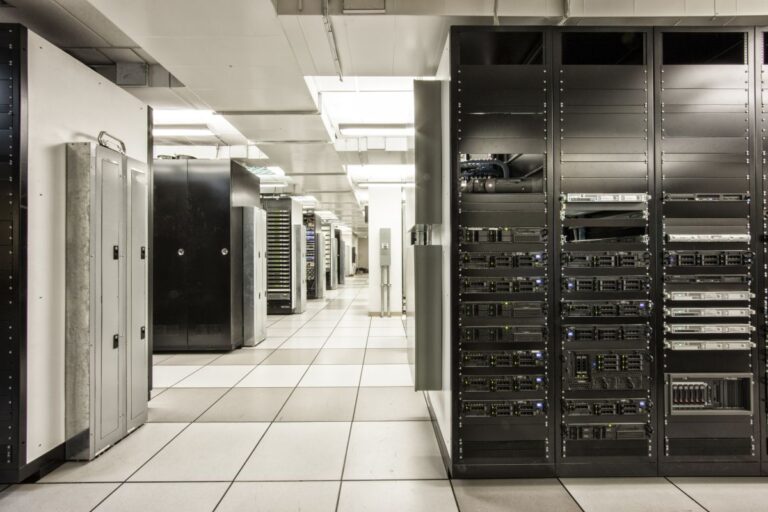 Wide-angle view of a data center interior with rows of black and silver server racks under bright fluorescent lighting. Above the image, bold text reads "U.S. Data Center Power Demand Could Reach 106 GW by 2035," highlighting concerns about growing energy consumption in digital infrastructure.