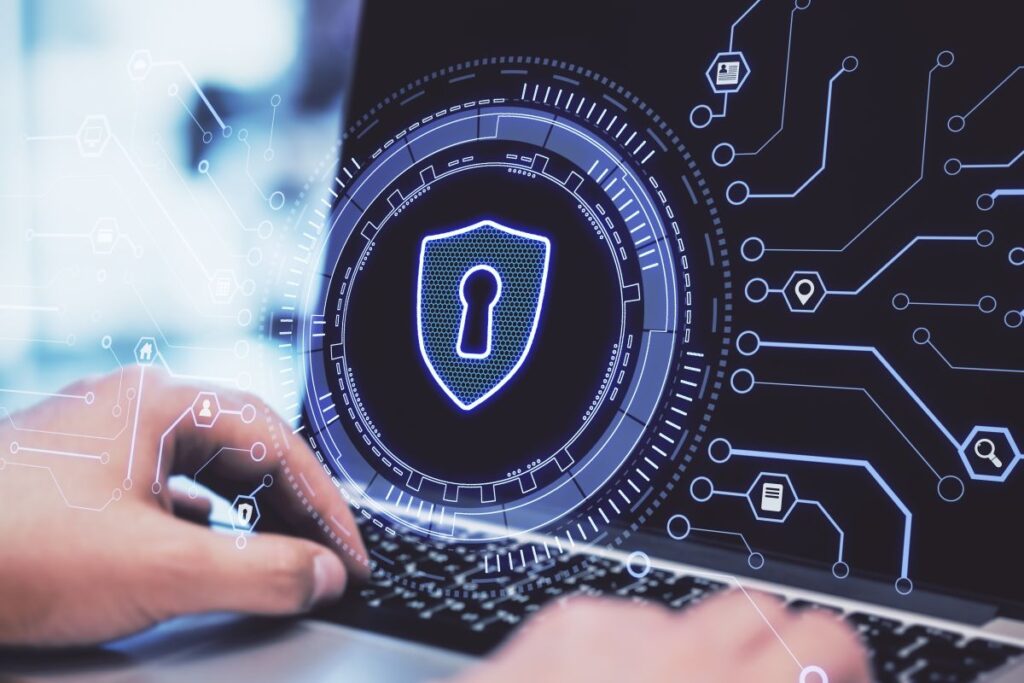 Person typing on a laptop with a glowing digital shield and keyhole displayed on the screen surrounded by circuit style interface graphics. Visual concept of cyber security protecting computer systems and network data from digital threats.