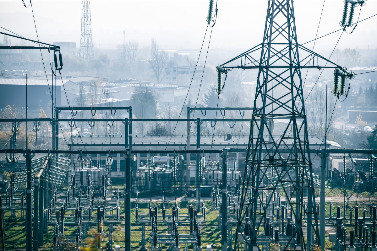 Power transmission station Electrical substation and transmission towers in a foggy industrial area supplying power to nearby buildings.