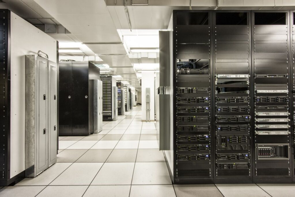 Storage racks aligned in a computer server room Black server racks line a bright computer server room with white floor tiles and overhead lighting.
